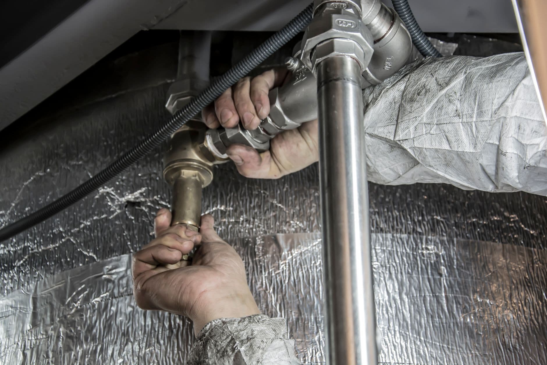 A plumber working under a sink with a pipe wrench