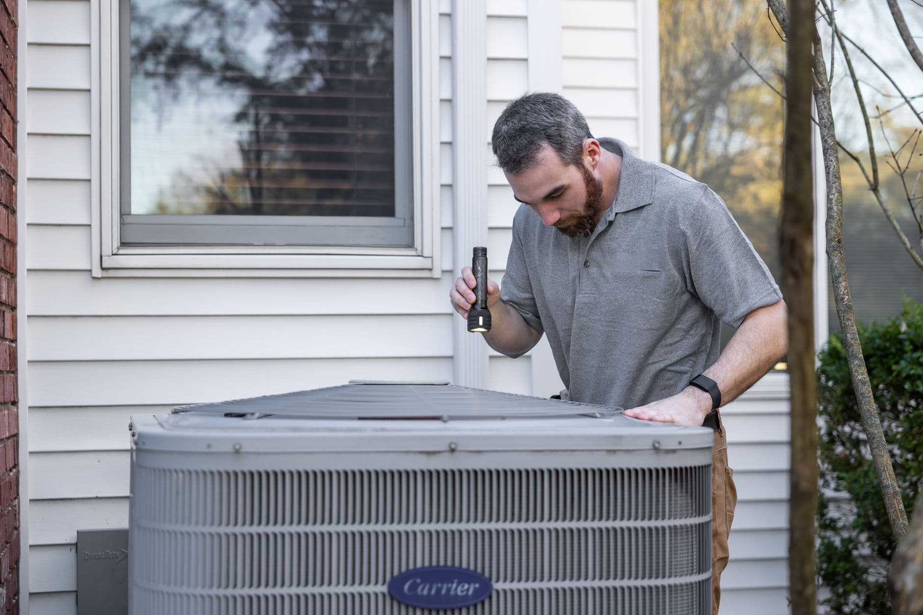 An HVAC technician working on an outdoor condenser unit